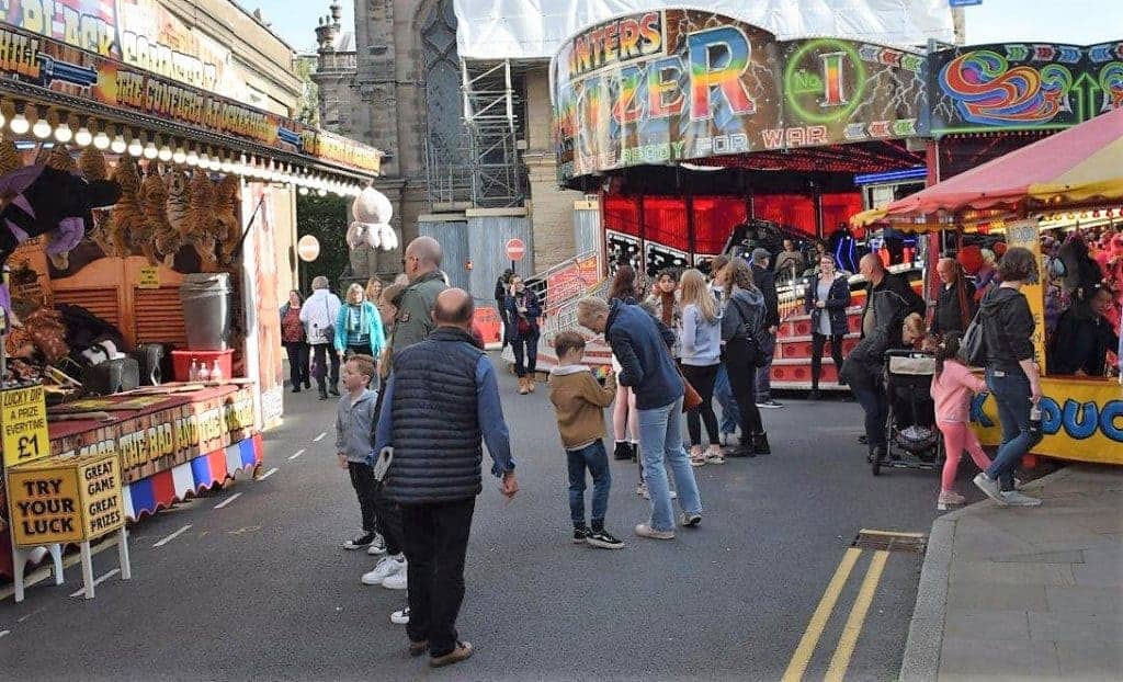 Photo of Newcomer to the fair this year’s first Mop, Denzil Danter’s Waltzer in front of a scaffolding-clad Mary’s Parish Church.